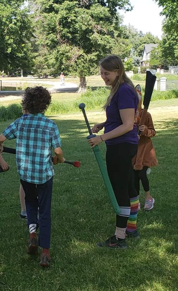 Our founder is shown with several children holding boffer swords during a camp event.